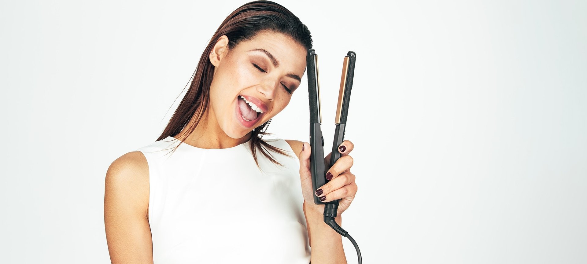 Junge Frau glättet ihre langen dunklen haare mit einem Glätteisen