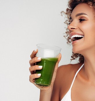 Lachende junge Frau mit Lockenfrisur und Smoothie Drink in der Hand