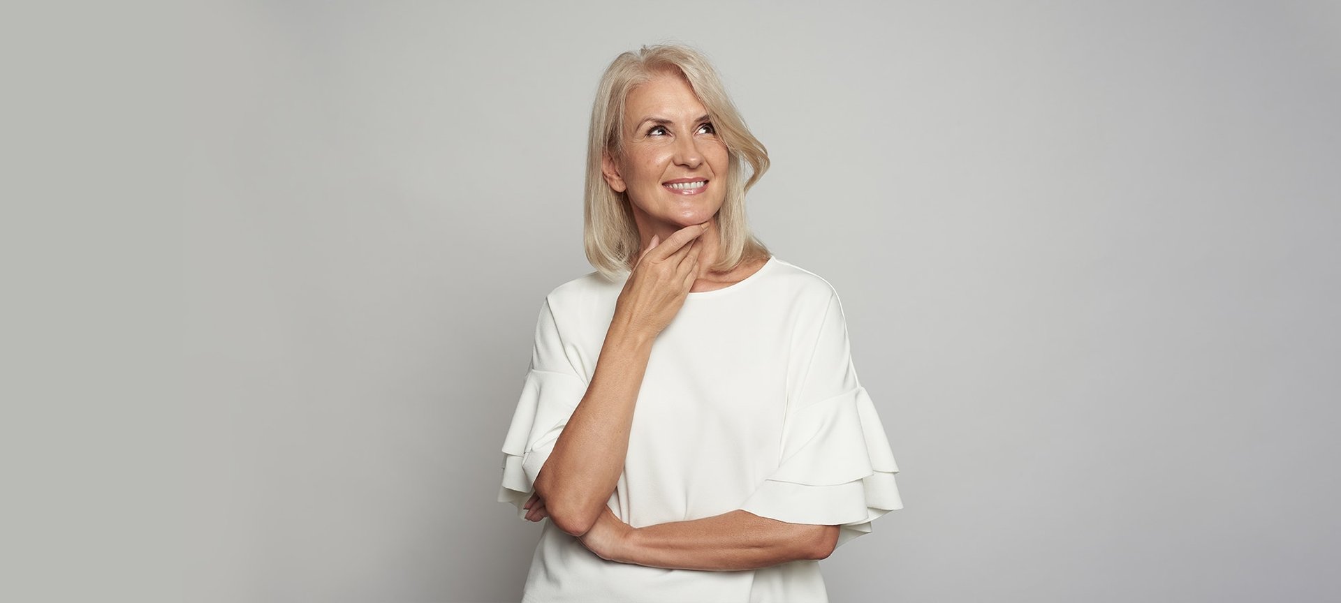 Frau vor grauer Wand lächelt und schaut in die Ferne