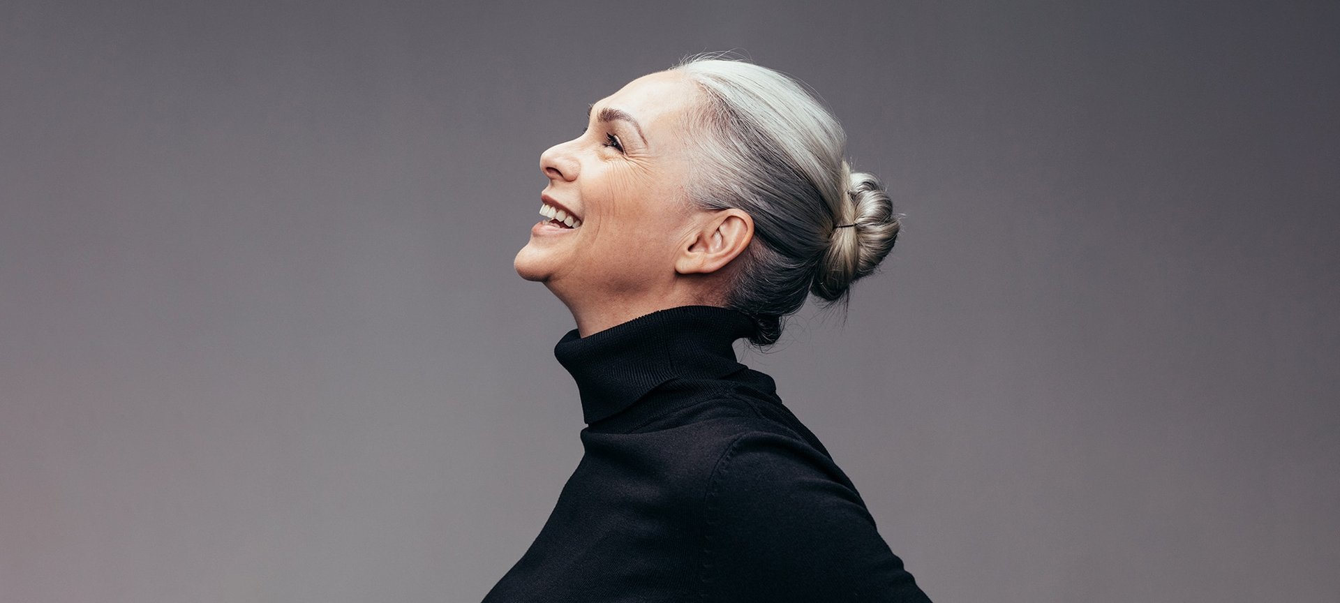 Frau im Profil mit grauen Haaren schaut lächelnd nach oben