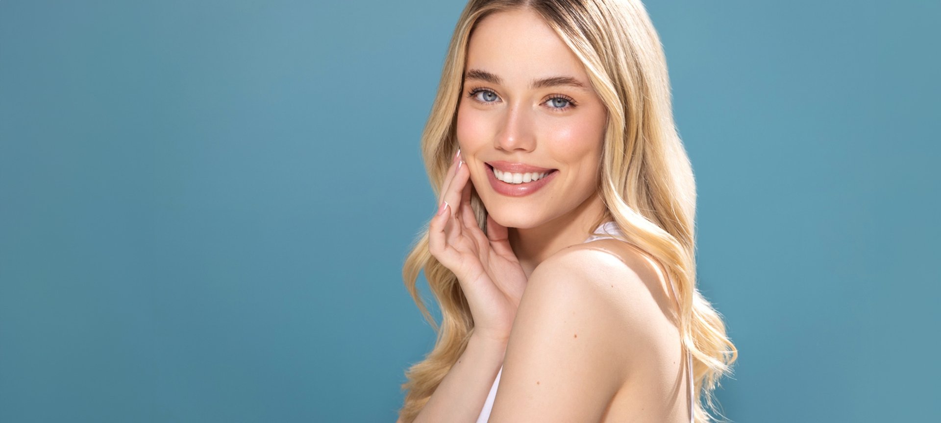 Eine junge Frau mit langen blonden Haaren schaut lächelnd links über ihre Schulter hinweg