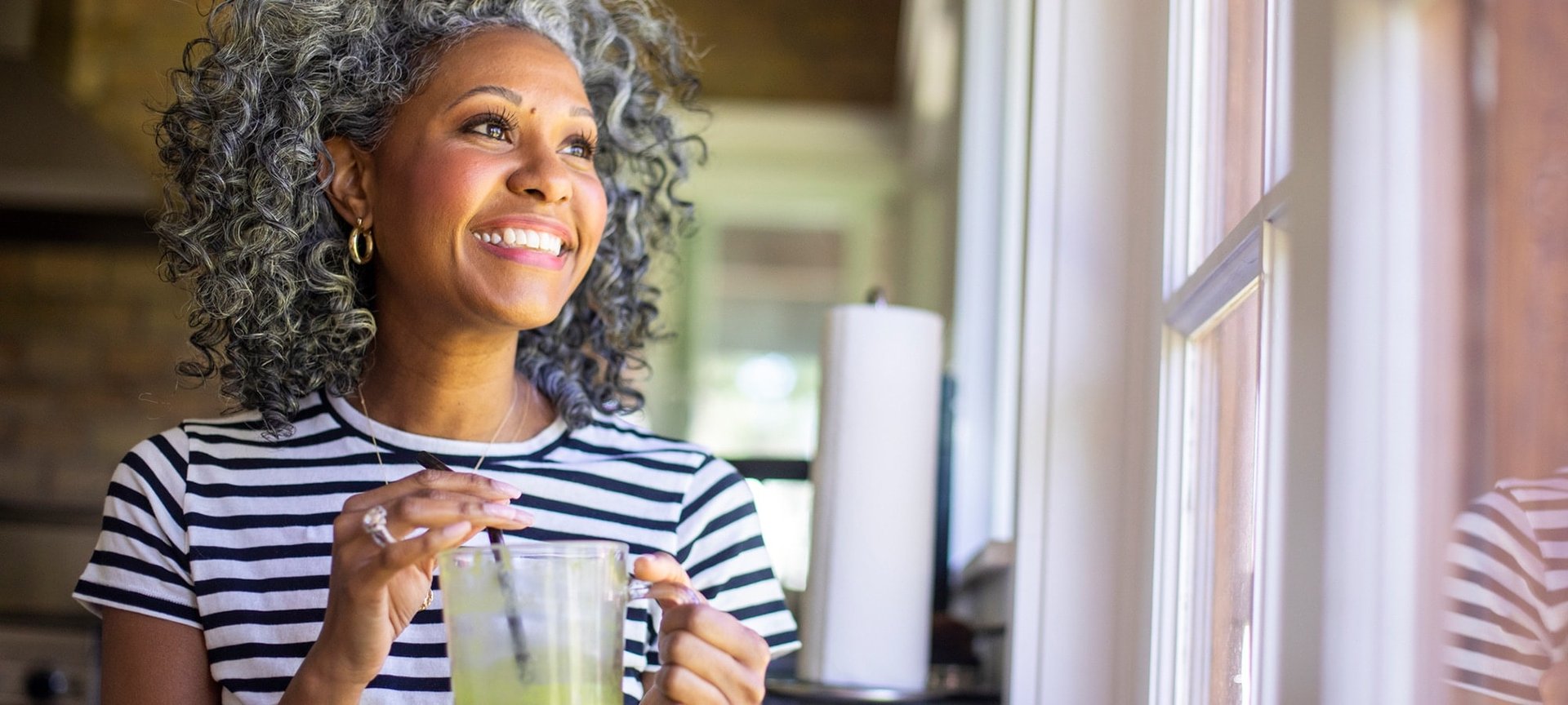 Lächelnde Frau mit lockigem silbergrauen Haaren schaut aus dem Fenster