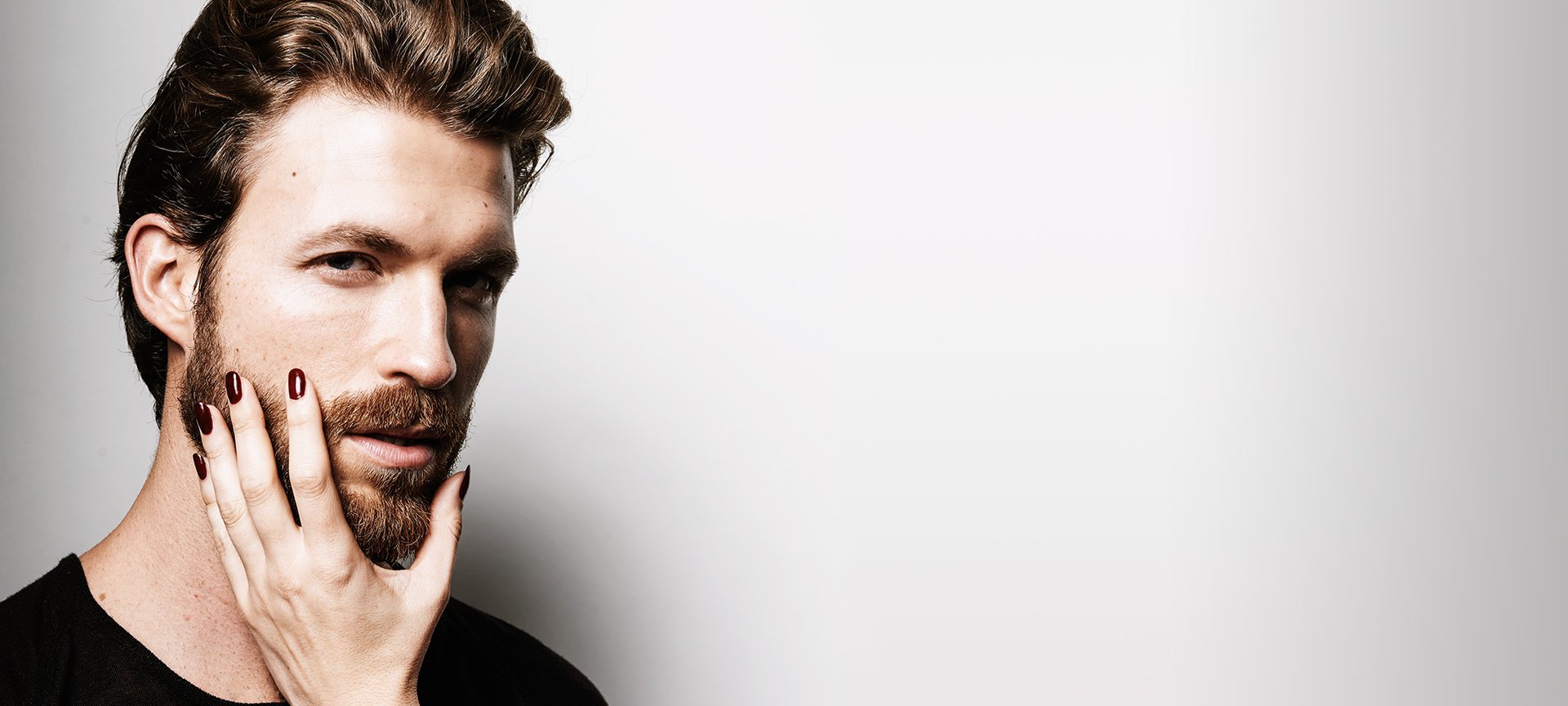 Mann mit getrimmten Bart wird von Frauenhand im Gesicht berührt