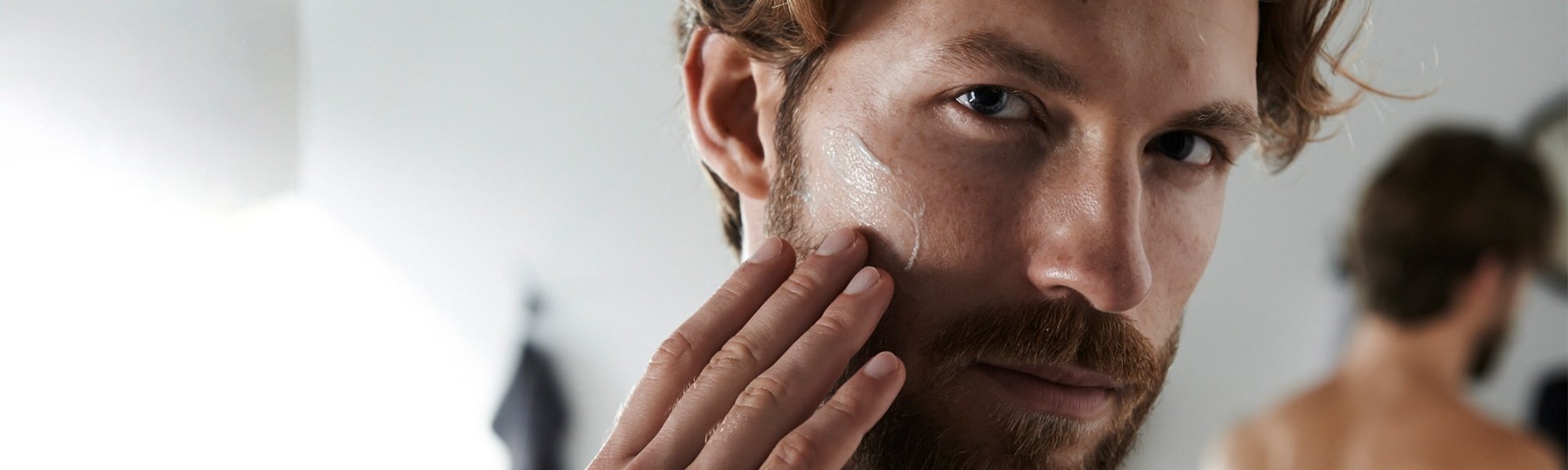 Ein junger Mann betrachtet sich im Spiegel und streicht sich dabei über seinen Bart