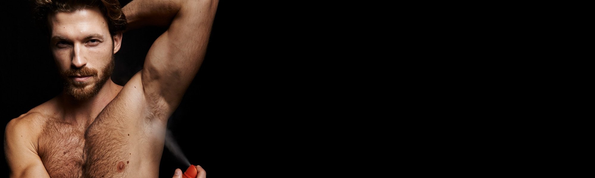 Ein Mann mit freiem Oberkörper sprüht ein Deo in seinen Achselbereich