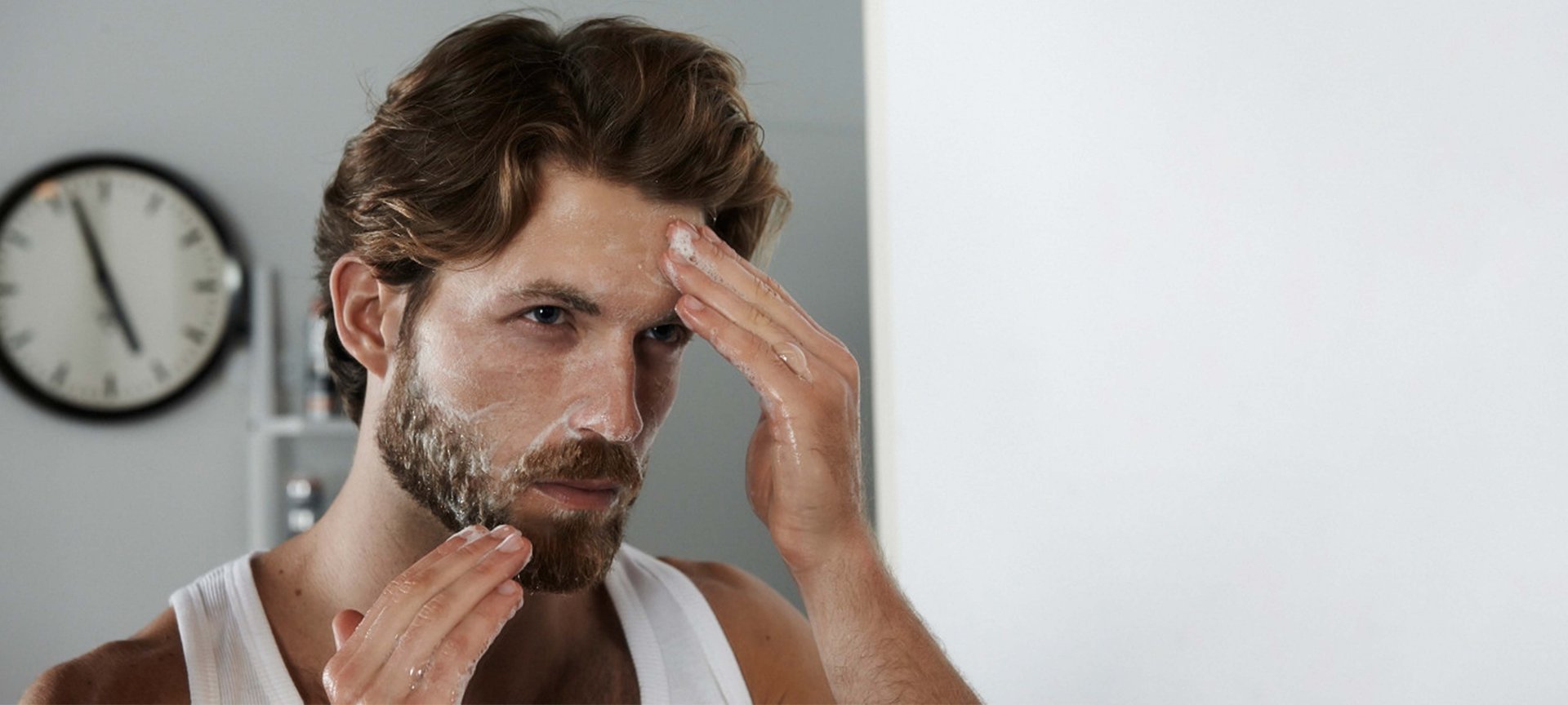 Ein Mann cremt sein Gesicht ein vor dem Spiegel stehend