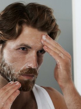 Ein Mann cremt sein Gesicht ein vor dem Spiegel stehend