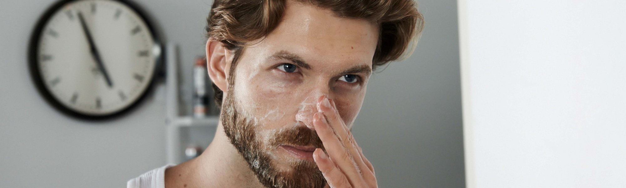 Ein Mann steht vor dem Spiegel und cremt sich seinen Nasenbereich ein