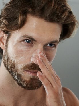 Ein Mann steht vor dem Spiegel und cremt sich seinen Nasenbereich ein