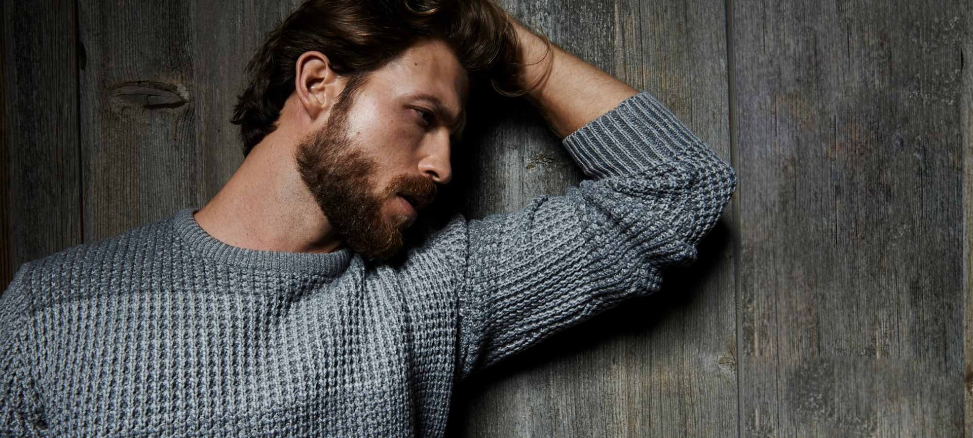 Ein Mann mit Bart seitlich an eine Wand gelehnt