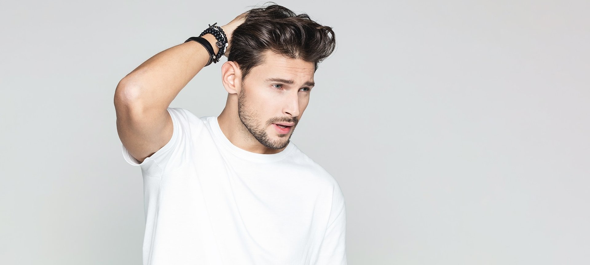 Junger Mann mit weißem Shirt streicht sich durch seine gestylten Haare