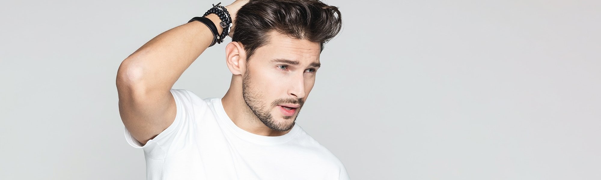 Junger Mann mit weißem Shirt streicht sich durch seine gestylten Haare