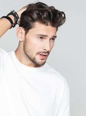 Junger Mann mit weißem Shirt streicht sich durch seine gestylten Haare