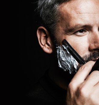 Mann vor schwarzem Hintergrund rasiert sich mit einem Rasiermesser