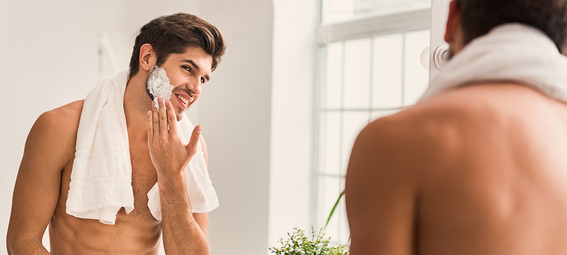 Ein Mann steht vor einem Spiegel und und verteilt Rasierschaum im Gesicht