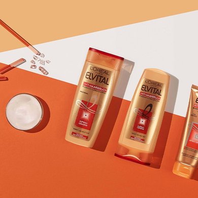 Ein zerbrochenes Glasstäbchen und eine Cremedose liegen neben drei Produkten der Anti-Haabruch-Reihe und zwei orangenen Würfeln