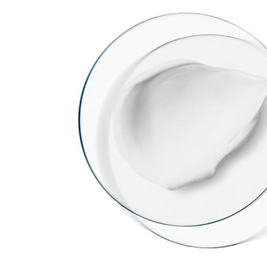 Petrischale mit weißer Creme neben grünen Pflanzenblättern