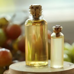 Zwei kleine Fläschchen mit Traubenkernöl, dahinter Weintrauben