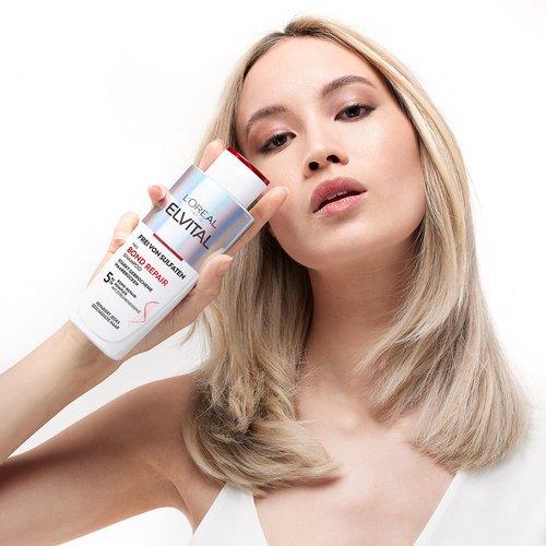 Model haelt sich eine Elvital Bond Repair Shampoo Verpackung vor ihr Gesicht