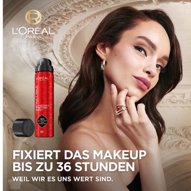 Model posiert vor einem Hintergrund mit Pariser Stuckverzierungen. Daneben ein Packshot eines Fixiersprays 'FIXIERT DAS MAKEUP BIS ZU 36 STUNDEN: weil wir es uns wert sind.'