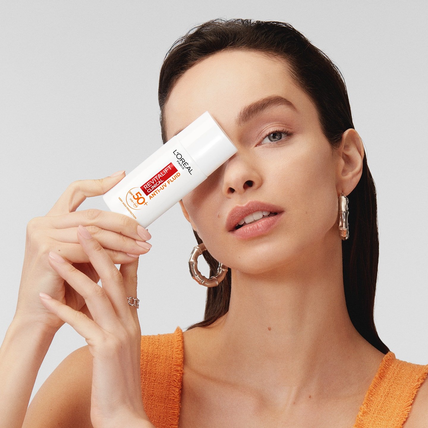 Eine junge Frau hält das REVITALIFT CLINICAL TÄGLICHE ANTI-UV FLUID LSF 50+ vor ihre rechte Gesichtshälfte