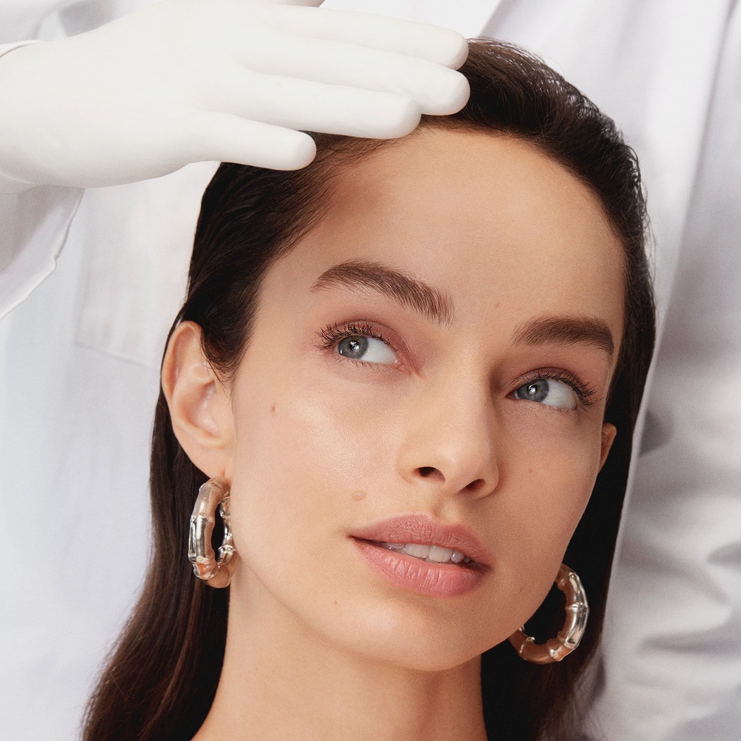 Gesicht einer jungen Frau am Kinn und Stirn gehalten von Händen in weißen Handschuhen