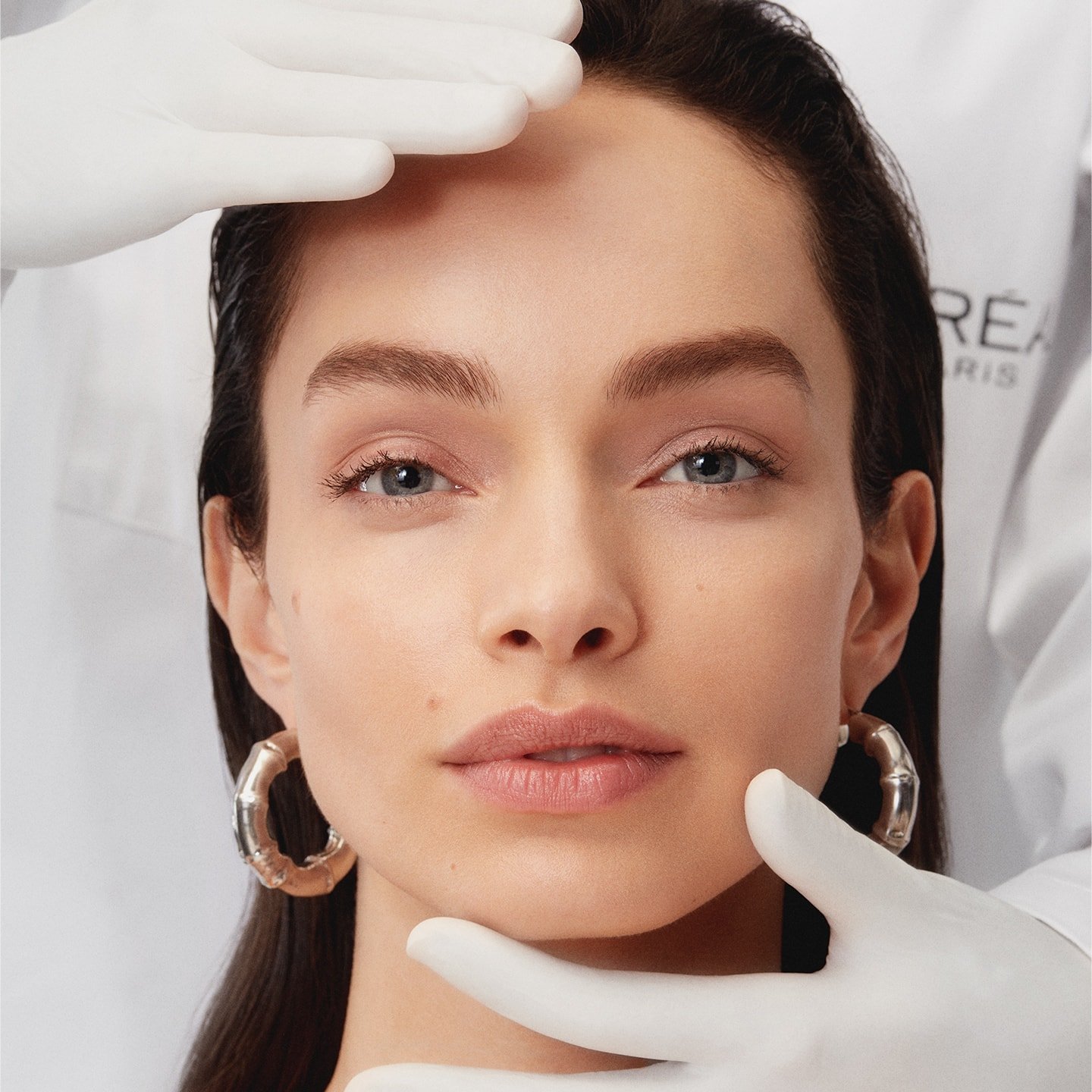 Gesicht einer jungen Frau am Kinn und Stirn gehalten von Händen in weißen Handschuhen